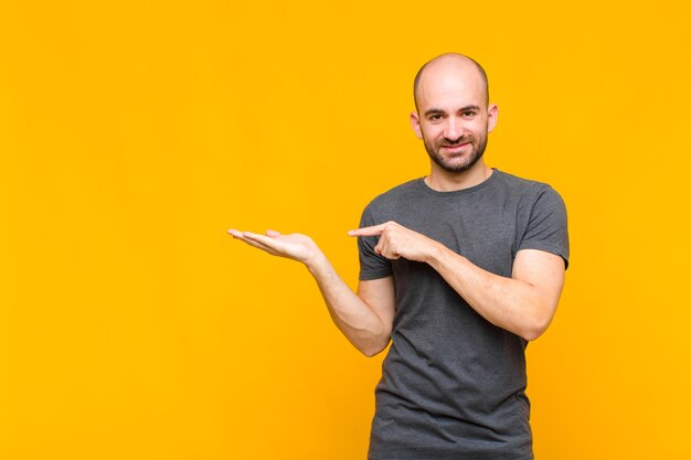 Careca sorrindo, sentindo-se feliz, despreocupado e satisfeito, apontando para um conceito ou ideia no espaço da cópia ao lado