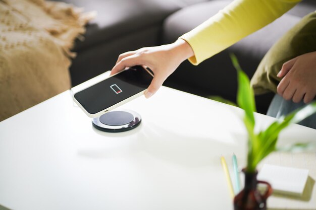 Carga de la batería del teléfono móvil con dispositivo de carga inalámbrico en la mesa Smartphone cargando en una plataforma de carga Teléfono móvil cerca del cargador inalámbrico Concepto de tecnología de estilo de vida moderno
