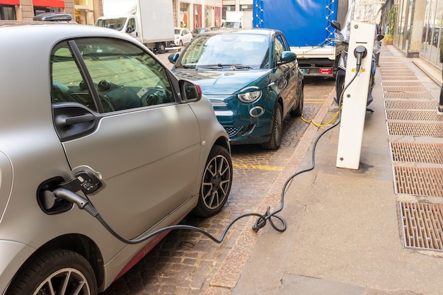 Foto carga de un pequeño coche eléctrico gris y verde en una calle de la ciudad