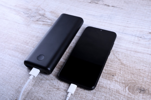 Carga de teléfono, powerbank carga teléfono inteligente, teléfono celular con banco de energía. Profundidad de campo en Power Bank en mesa de madera