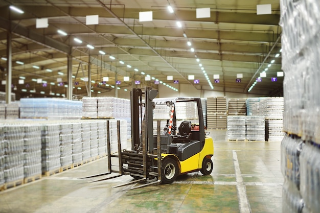 Foto cargador amarillo en el fondo de un enorme almacén industrial de alimentos con botellas de plástico pet con cerveza, agua, bebidas.