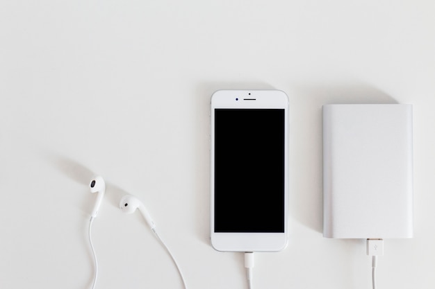 Foto cargador de banco de energía con teléfono inteligente y auricular en fondo blanco