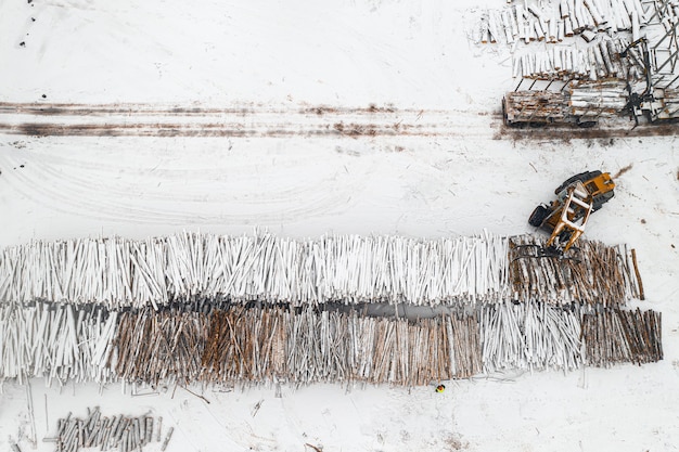 Cargador carga troncos apilados en montones cubiertos de nieve