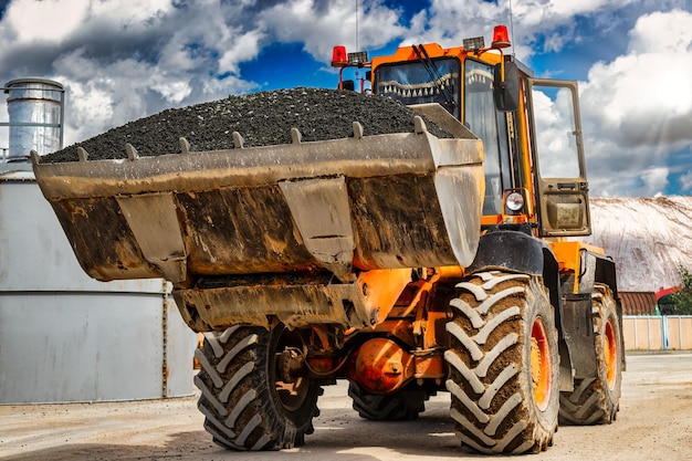 Un cargador frontal grande transporta piedra triturada o grava en un balde en un sitio de construcción o planta de concreto Transporte de materiales a granel Equipos de construcción Transporte de carga a granel