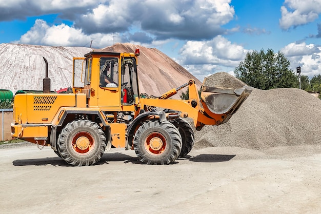 Un cargador frontal grande transporta piedra triturada o grava en un balde en un sitio de construcción o planta de concreto Transporte de materiales a granel Equipos de construcción Transporte de carga a granel