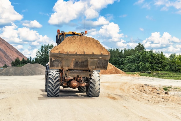 Un cargador frontal grande transporta piedra triturada o grava en un balde en un sitio de construcción o planta de concreto Transporte de materiales a granel Equipos de construcción Transporte de carga a granel