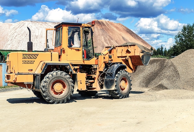 Un cargador frontal grande transporta piedra triturada o grava en un balde en un sitio de construcción o planta de concreto Transporte de materiales a granel Equipos de construcción Transporte de carga a granel