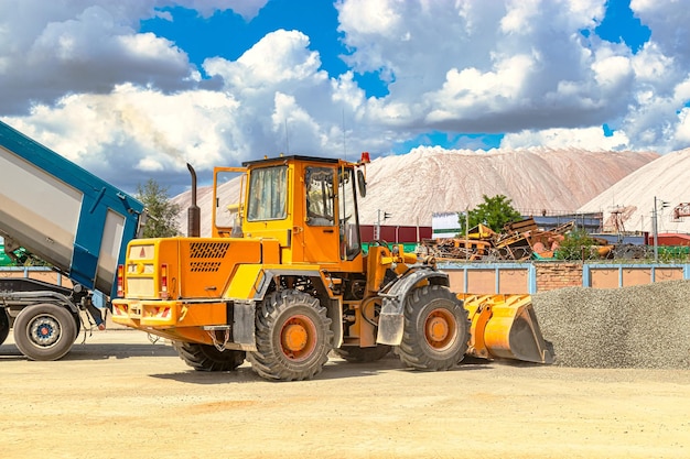 Un cargador frontal grande transporta piedra triturada o grava en un balde en un sitio de construcción o planta de concreto Transporte de materiales a granel Equipos de construcción Transporte de carga a granel