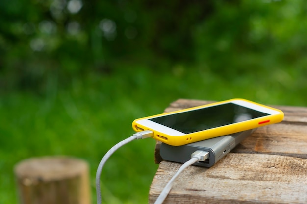 Cargador de viaje portátil. Power Bank carga un teléfono inteligente en una mesa de madera, en el fondo de la naturaleza. Concepto sobre el tema del turismo.