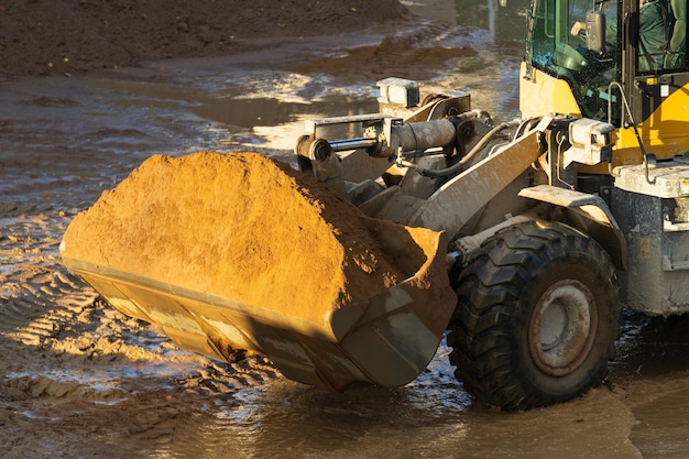 Cargadora de ruedas delanteras del tractor con arena en la cuchara, obras de movimiento de tierras en el concepto de sitio de construcción