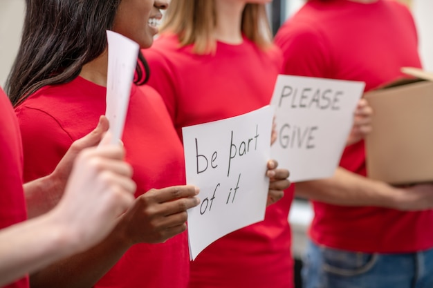 Caridad. Manos de voluntarios en camisetas rojas sosteniendo carteles que piden la participación en la caridad