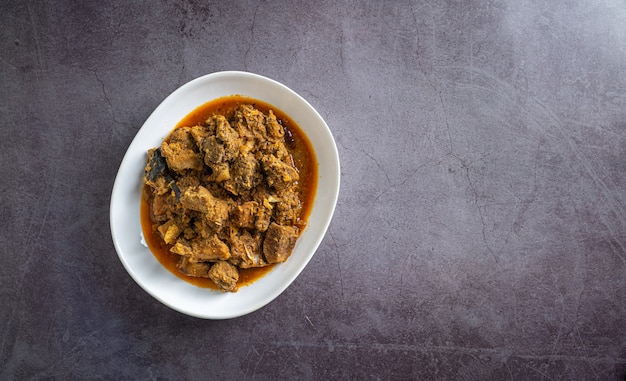 Caril de carne picante servido em uma tigela branca na vista superior do pano de fundo de ardósia preta