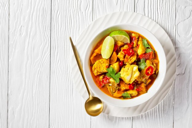 Caril de peixe marisco brasileiro Moqueca Baiana com leite de coco de peixe branco vários legumes fatias de limão e coentro fresco em uma tigela branca em uma mesa branca espaço livre