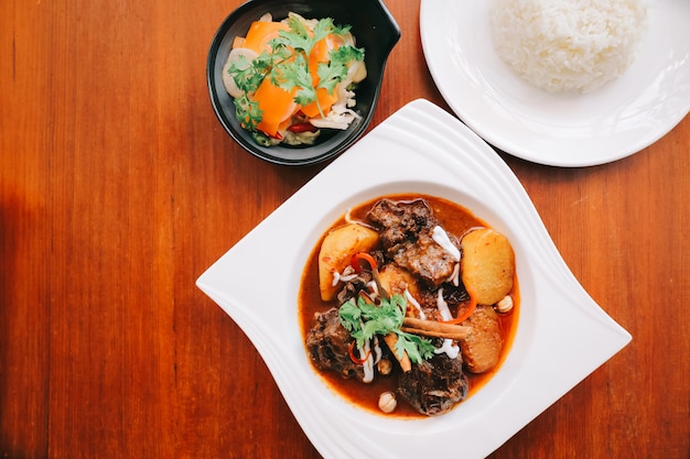 Caril massaman de carne com arroz e salada em fundo de madeira, comida tailandesa