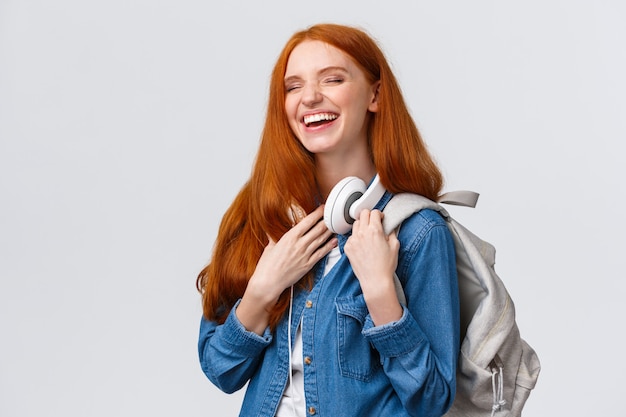 Carismática y alegre, encantadora pelirroja amigable que se ríe de una broma de novia mientras regresaba del campus de las clases universitarias, se divierte riéndose con los ojos cerrados, sonriendo y sosteniendo la mochila