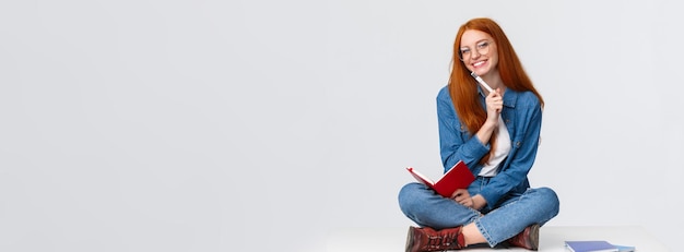 Foto carismática e simpática garota ruiva sonhando em fazer anotações ou preparar o dever de casa enquanto está sentado na fl