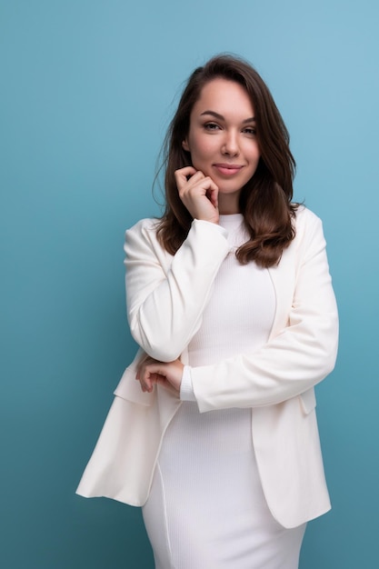 Carismática jovem morena de vestido branco flertando no fundo do estúdio