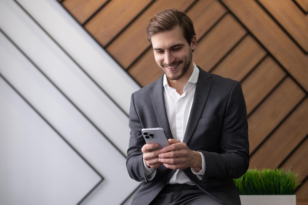 Carismático jovem empresário com um telefone nas mãos com um sorriso no escritório