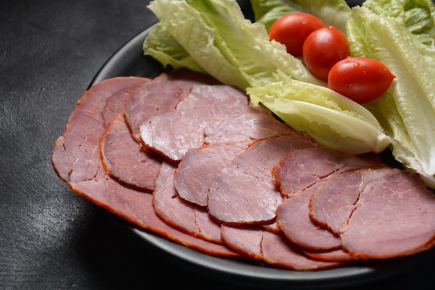 Carne ahumada en rodajas con tomates cherry y lechuga en placa negra