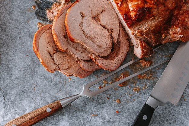 Carne al horno en una bandeja para hornear y papel pergamino junto a un tenedor para carne