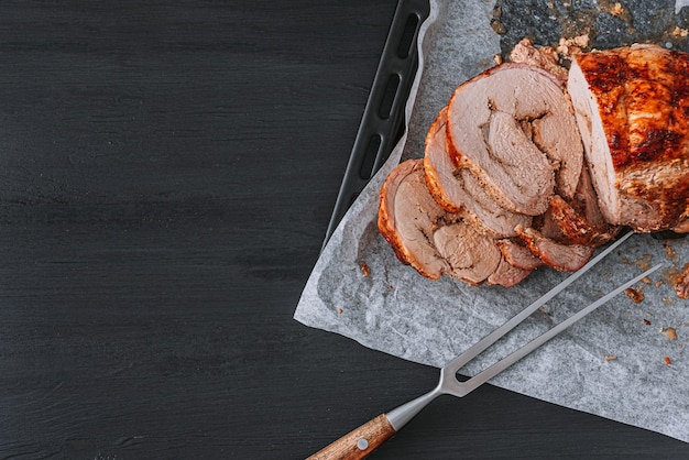 Carne al horno en una bandeja para hornear y papel pergamino junto a un tenedor para carne