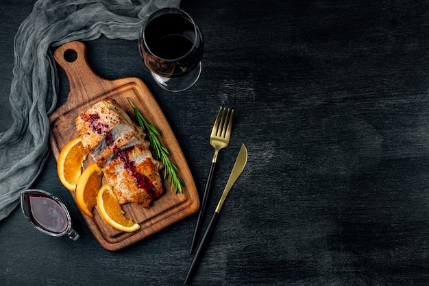 Carne al horno con salsa de arándanos rojos y una copa de vino en negro, vista superior