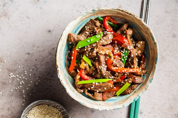 Carne asiática do teriyaki com cebolas verdes e sementes de gergelim na bacia bonita, fundo cinzento, vista superior.