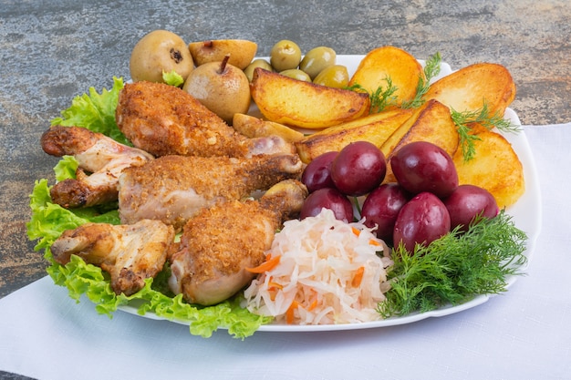 Carne assada e batata ao lado de vegetais em conserva em um prato sobre um pano.