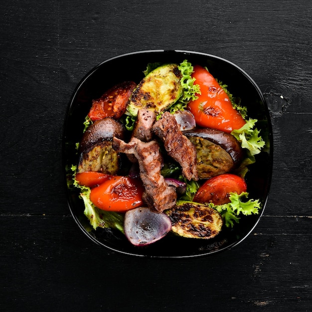 Carne assada e legumes grelhados em um prato preto Em um fundo de madeira Vista superior Espaço livre para o seu texto