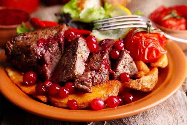 Foto carne assada saborosa com salada de molho de cranberry e legumes assados no prato fundo de madeira