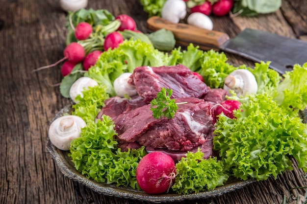 Carne bovina crua com vegetais frescos. Bife fatiado em rabanetes de saladas de alface e cogumelos.