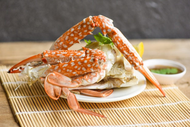Carne de cangrejo - garras y patas de cangrejo cocidas en un plato blanco y salsa de mariscos en la mesa, cangrejo azul nadando