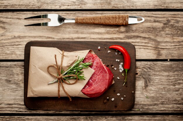 carne de una carnicería envuelta en papel. Un trozo de carne en madera con diferentes especias en un estilo rústico.