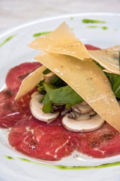 Carne carpaccio com parmesan queijo arugula e cogumelos em prato branco deli comida