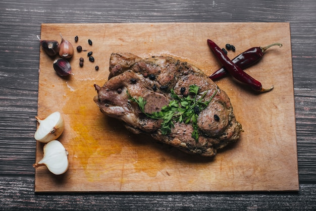 Carne de cerdo cocida en una tabla de cortar sobre una mesa con pimiento, ajo, cebolla y especias.