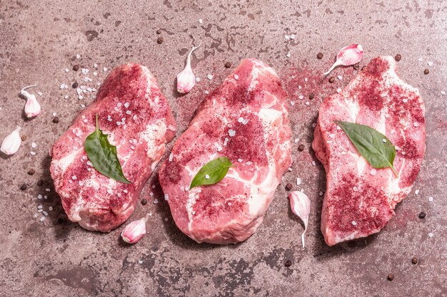 Carne de cerdo cruda, cortes en rodajas. Carne fresca, zumaque seco, ajo y hojas de albahaca. Concepto de comida de cocina saludable, luz dura de moda, sombra oscura. Fondo de piedra de mármol, vista superior