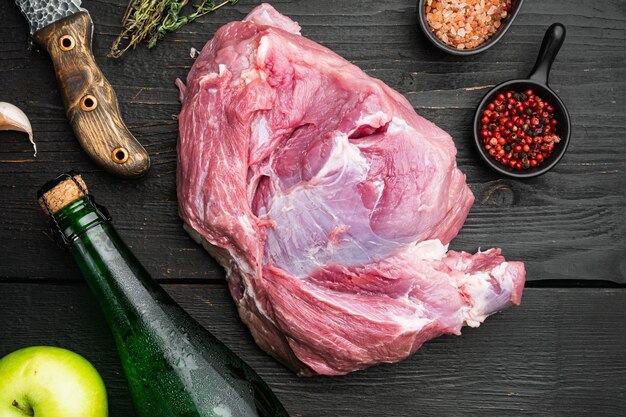 Carne de cerdo cruda e ingredientes para asado, con sidra seca de manzana, sobre fondo de mesa de madera negra, vista superior plana