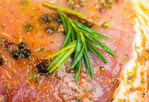 Carne de cerdo cruda con especias y hierba de romero verde. Fondo de textura de carne roja, jamón crudo. Fotografía macro. Carne jugosa fresca grasa.