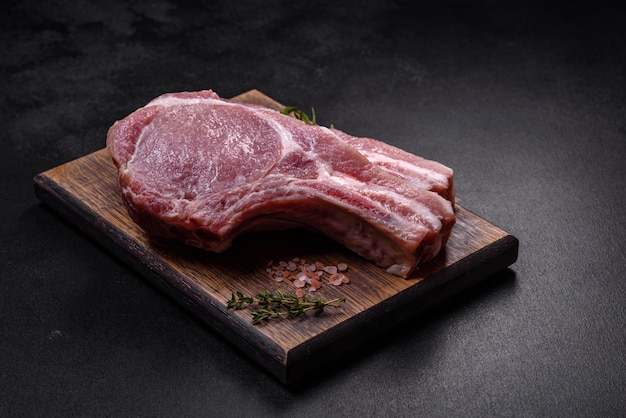 Carne de cerdo cruda fresca en las costillas con especias y hierbas en una tabla de cortar de madera sobre un fondo de hormigón oscuro
