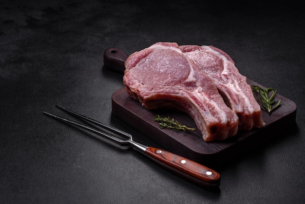 Carne de cerdo cruda fresca en las costillas con especias y hierbas en una tabla de cortar de madera sobre un fondo de hormigón oscuro