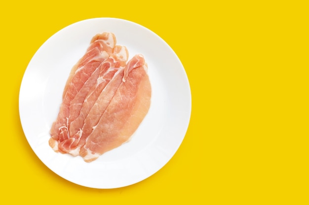 Carne de cerdo cruda en rodajas en un plato blanco sobre fondo amarillo.