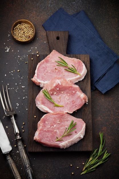 Carne de cerdo cruda sobre una tabla de cortar de madera sobre una pizarra, piedra u hormigón.