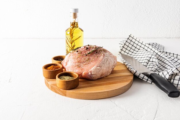 Carne de cerdo cruda en una tabla de cortar redonda con tazones de diferentes especias y aceite de romero para cocinar el concepto de cocinar carne