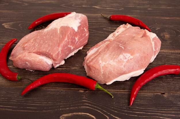 Foto carne de cerdo fresca cruda sobre un fondo de madera con primer plano de pimiento rojo picante