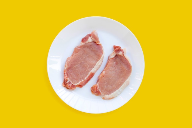 Carne de cerdo fresca en plato blanco sobre fondo amarillo.