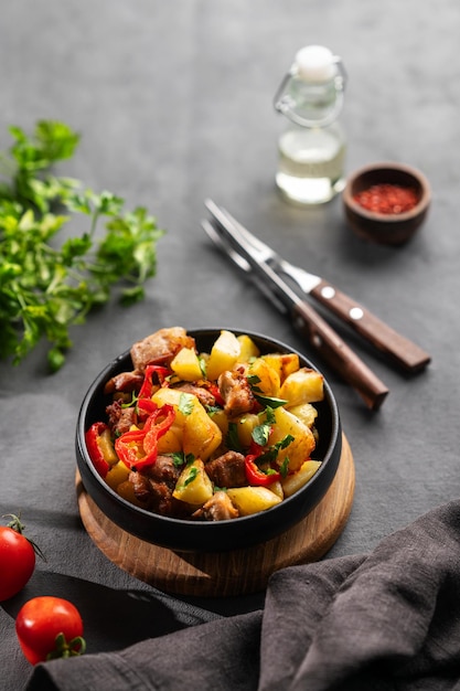 Carne de cerdo frita con patatas, cebollas y pimientos Plato nacional georgiano casero ojakhuri en una sartén negra sobre un fondo oscuro con tomates frescos, hierbas y sombras