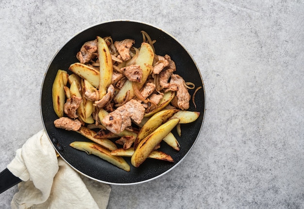 Carne de cerdo con patatas y cebollas en una sartén.