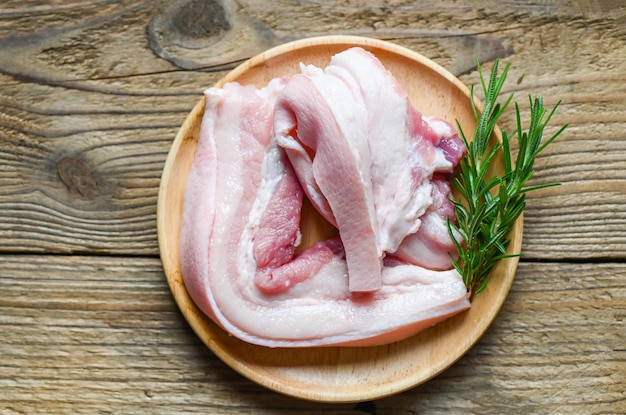 Carne de cerdo en un plato de madera con romero, carne de cerdo rayada cruda fresca para cocinar la vista superior de alimentos