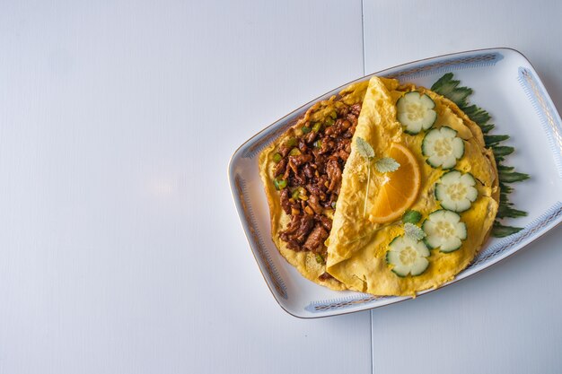 Carne cheia de omelete frito com legumes na mesa branca