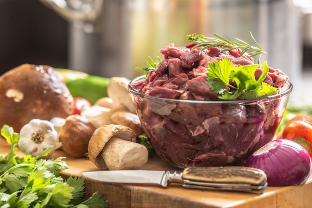 Carne de ciervo en rodajas preparada para guiso de setas del bosque de caza, hierbas, verduras y cuchillo.